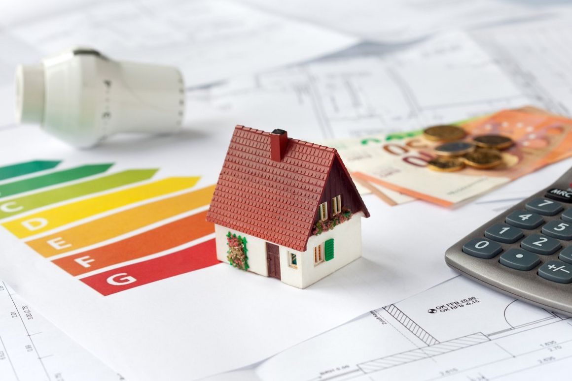 Modellhaus mit Energieausweis, Geld und Taschenrechner auf einem Bauplan.